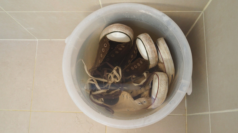 Old dirty black and white sneakers shoes with water in wash bucket.