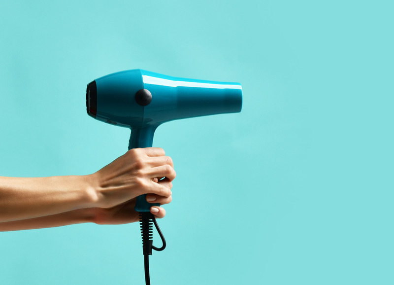 Woman hands hold blue hair dryer on mint blue